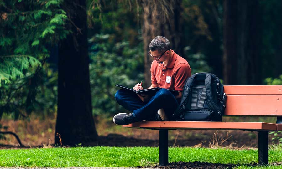 Student writes in journal outside on a bench
